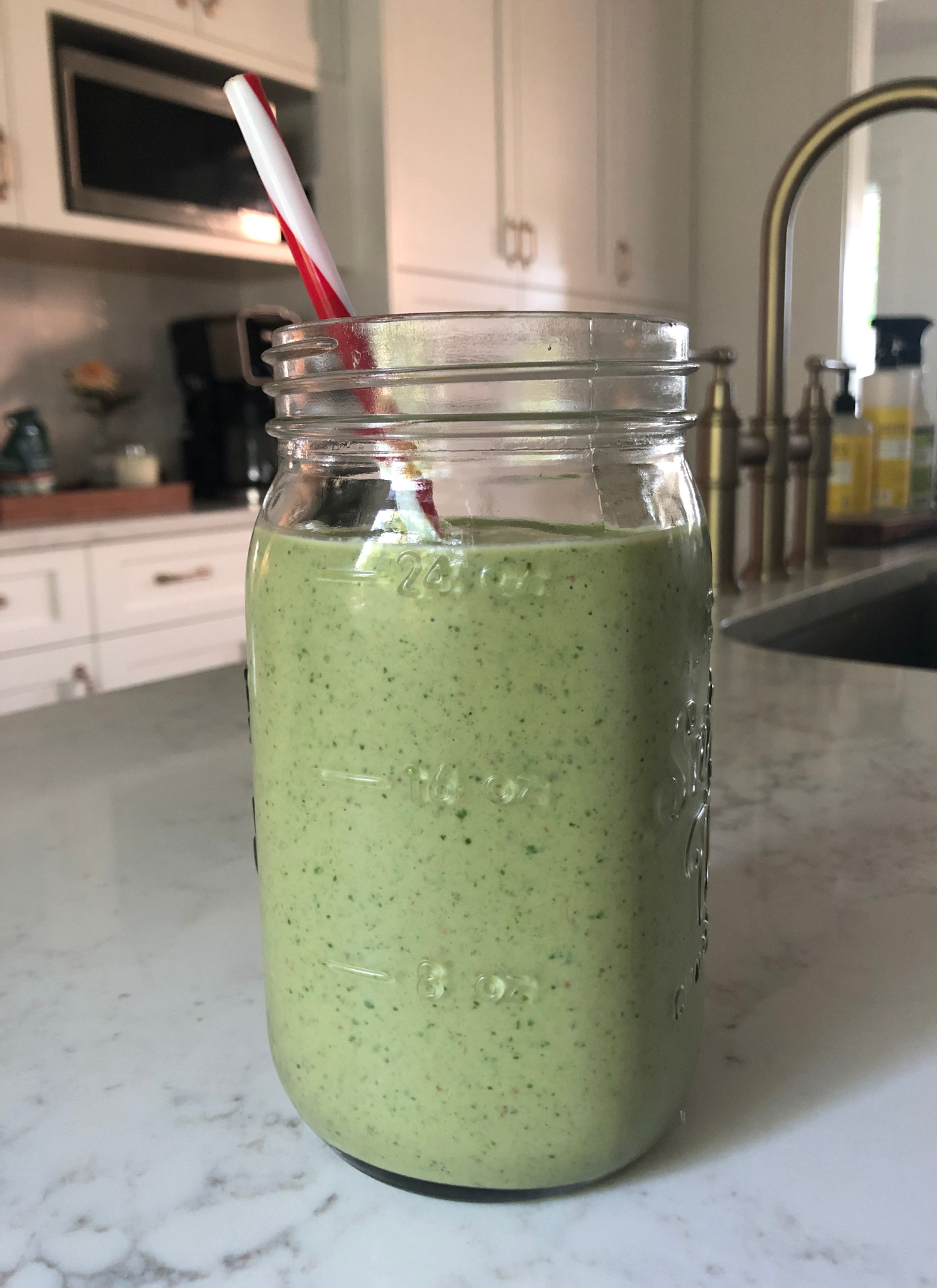 Green smoothie in glass jar with straw.