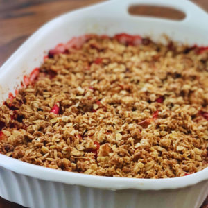 Baked Strawberry Rhubarb Crumble in white casserole dish on wooden table.
