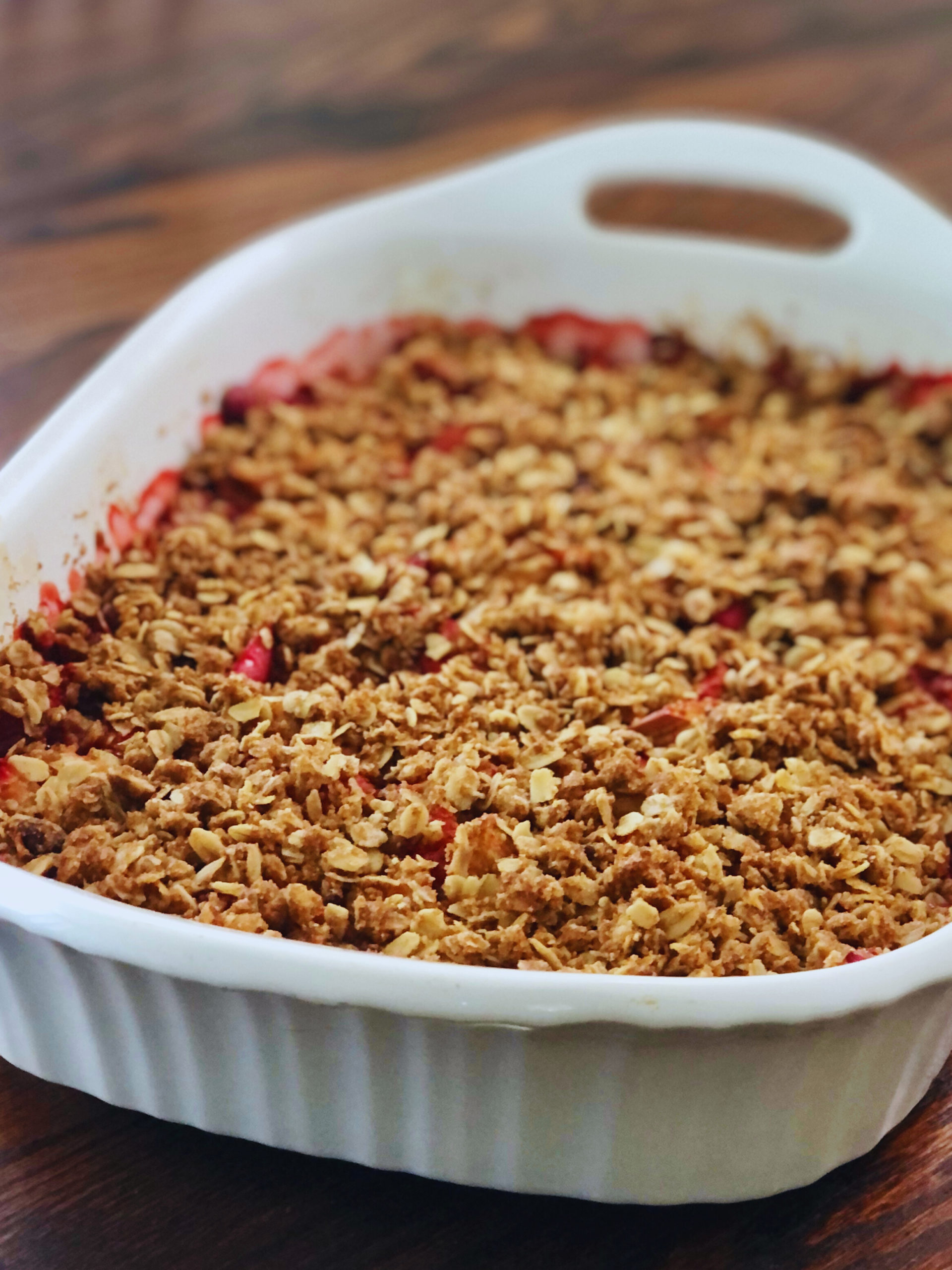 Baked Strawberry Rhubarb Crumble in white casserole dish on wooden table.
