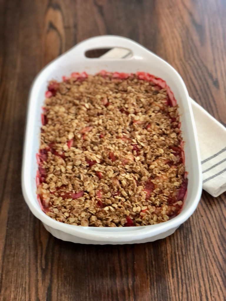 Baked crumble in white casserole dish on a dark wood table.